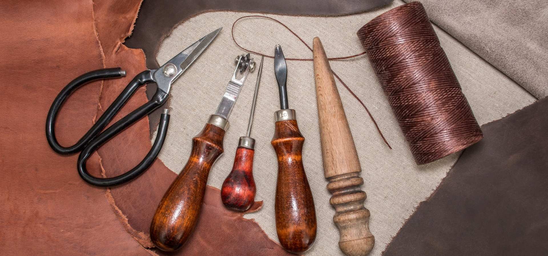 Essential leather craft tools and thread arranged on leather material
