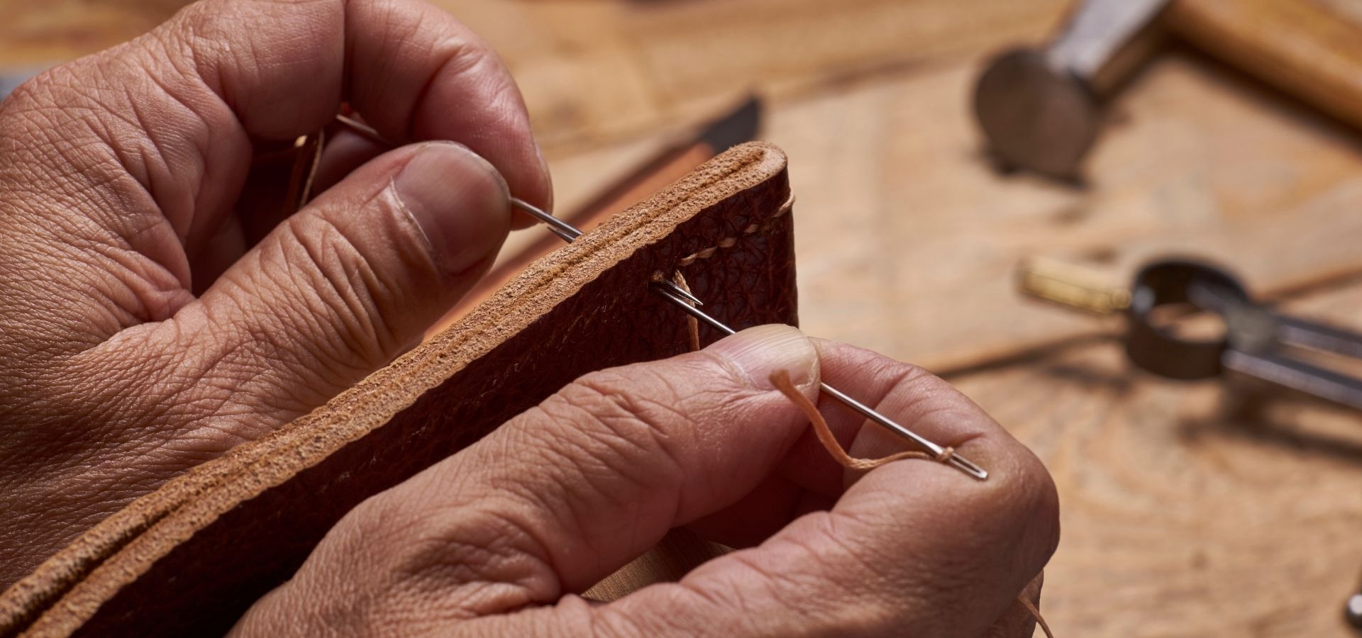 Hands stitching two pieces of leather together by hand for a leather craft product