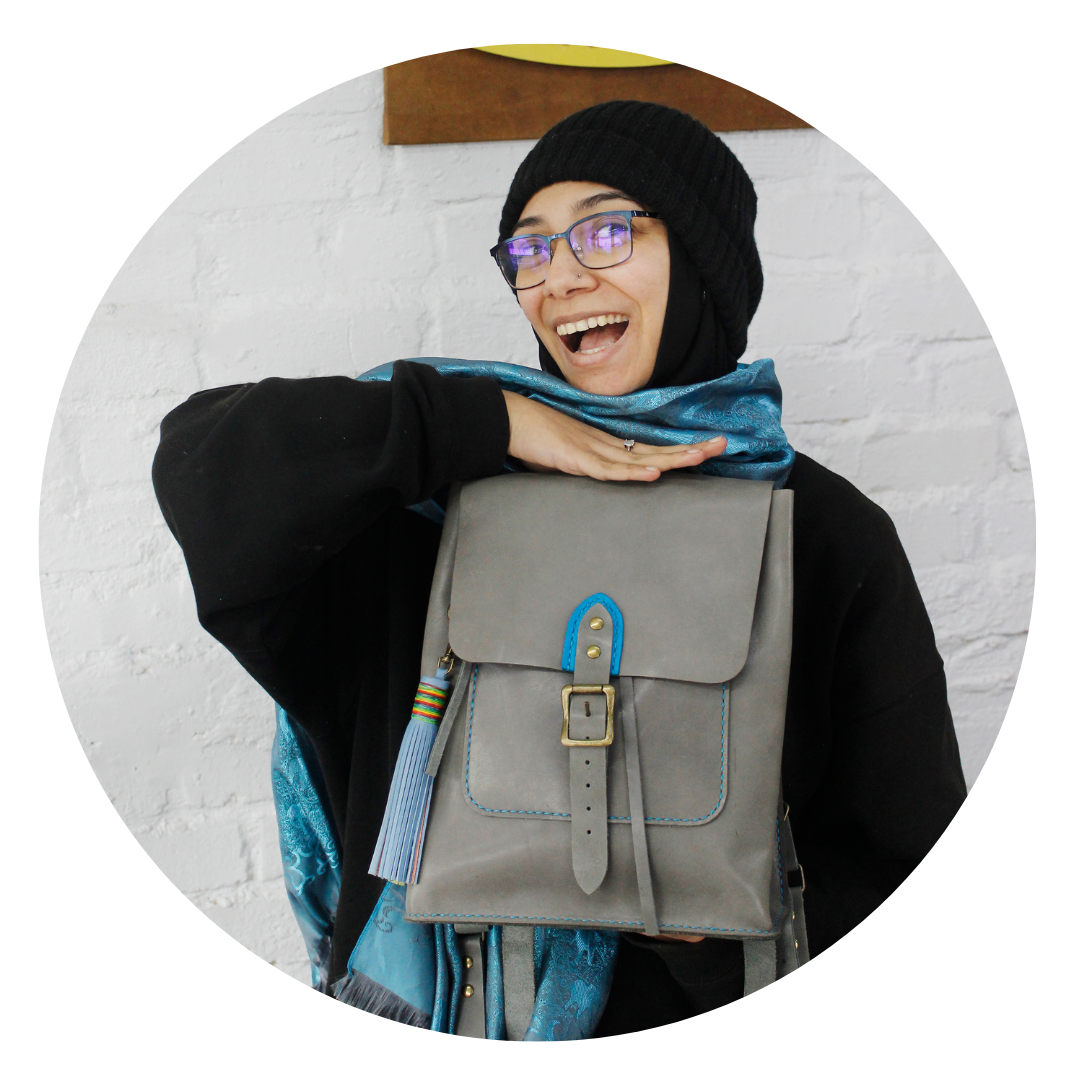 Smiling woman proudly displaying her handmade grey leather craft backpack