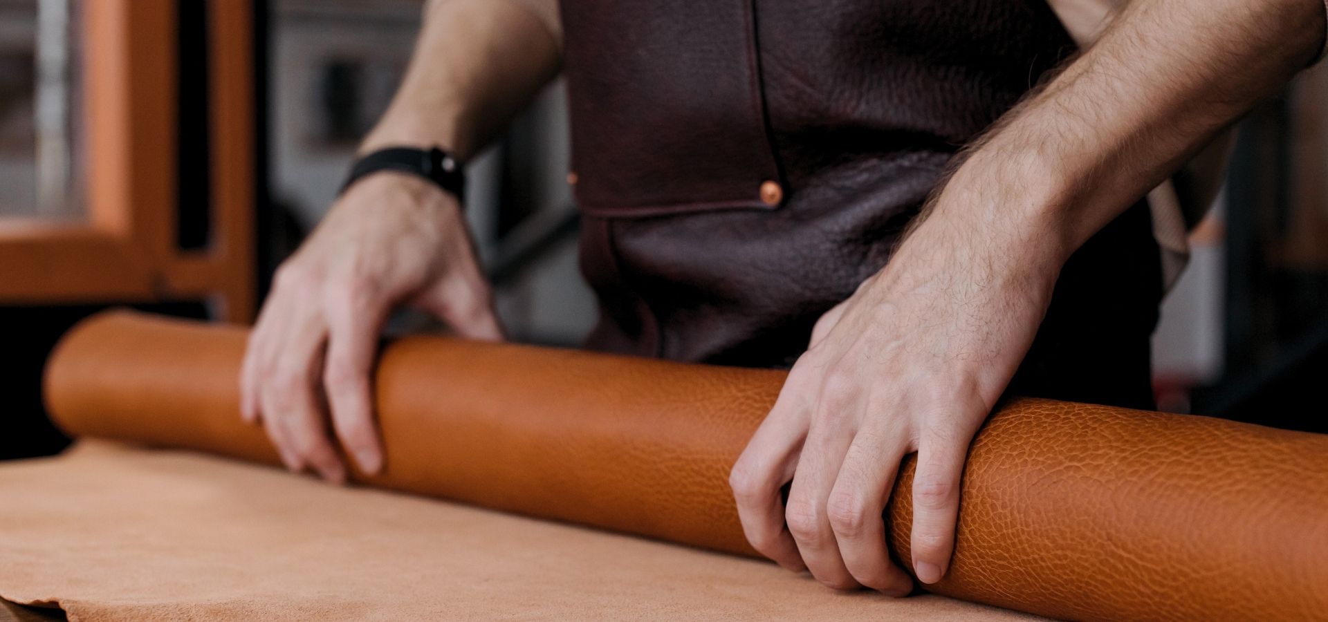 Person rolling a sheet of brown leather on a workbench for a leather craft project