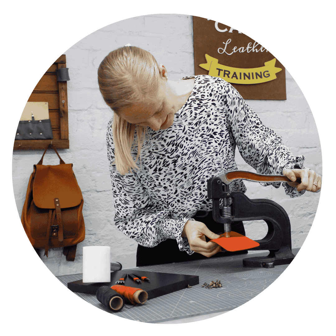 A leather craft instructor using a press machine to cut leather pieces at a Cape Town training workshop.