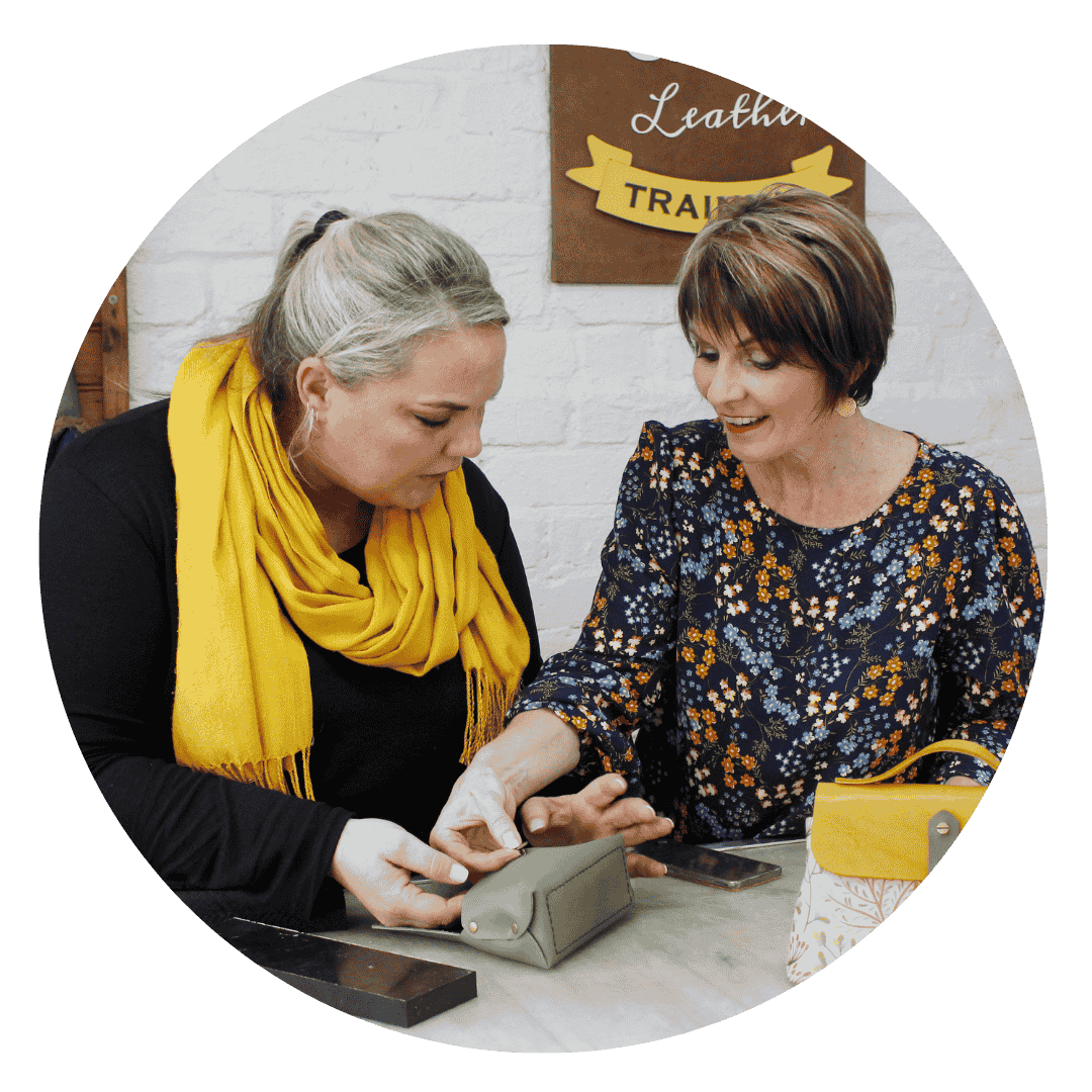 Two women assembling a small leather pouch together during a leather craft class focused on practical skills.